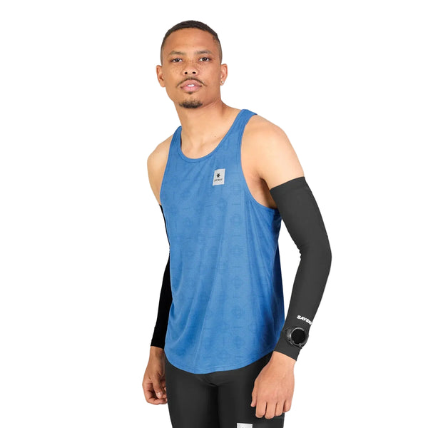 En mand iført en Saysky Reactive Flow Singlet, Herre, Blue Aop, samt sorte kompressionsærmer og sorte leggings, står med ansigtet vendt fremad foran en ensfarvet hvid baggrund. Den lette singlet er designet til optimal svedtransport, så han holder sig kølig og komfortabel under intens aktivitet.