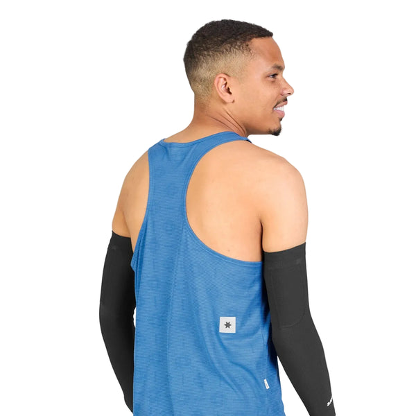 En mand, der står med ryggen til, iført den blå Saysky Reactive Flow Singlet, Herre, Blue Aop og sorte armærmer, står foran en ensfarvet hvid baggrund. Den ultralette singlet er designet til optimal svedtransport og sikrer komfort, mens han kigger over skulderen med et let smil.