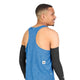 En mand, der står med ryggen til, iført den blå Saysky Reactive Flow Singlet, Herre, Blue Aop og sorte armærmer, står foran en ensfarvet hvid baggrund. Den ultralette singlet er designet til optimal svedtransport og sikrer komfort, mens han kigger over skulderen med et let smil.