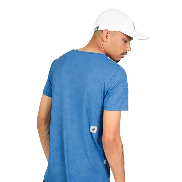 En person iført en blå Saysky Reactive Flow T-shirt, Herre, Blue Aop, og en hvid baseballkasket står med ryggen let vendt væk fra kameraet og kigger over sin venstre skulder. Baggrunden er helt hvid.