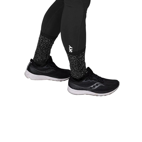 En person iført Saysky Reflective Combat Socks 300 (unisex, sort), sorte leggings og sorte løbesko med hvide såler står på en hvid baggrund.