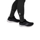 En person iført Saysky Reflective Combat Socks 300 (unisex, sort), sorte leggings og sorte løbesko med hvide såler står på en hvid baggrund.