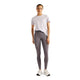 En person står med ansigtet vendt fremad iført en lyselilla T-shirt, hvide sportssko og New Balance Reflective RC Heat Legging 27″ til kvinder i farven Neptune Grey – leggings med NB HEAT-teknologi – foran en ensfarvet hvid baggrund, hvilket udgør et ideelt sæt tøj til løb i koldt vejr.