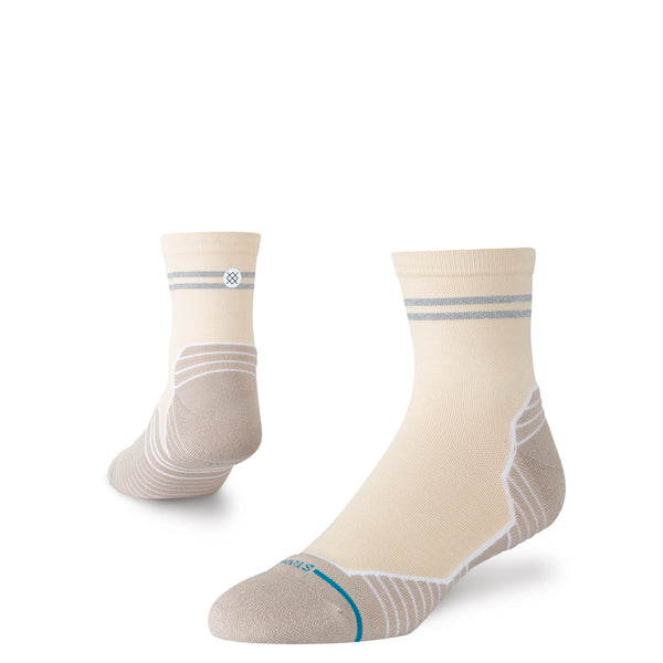 På billedet ses et par Stance Reflector Light Quarter unisex-sokker i farven »Croissant«, der er fremstillet i cremefarvet stof med grå striber ved manchetten og beige detaljer ved hæl og tå – den ene sok står oprejst, mens den anden er vinklet for at fremhæve siden og sålen. Disse sokker er designet som løbesokker og tilbyder enestående åndbarhed, så dine fødder forbliver komfortable under aktivitet.