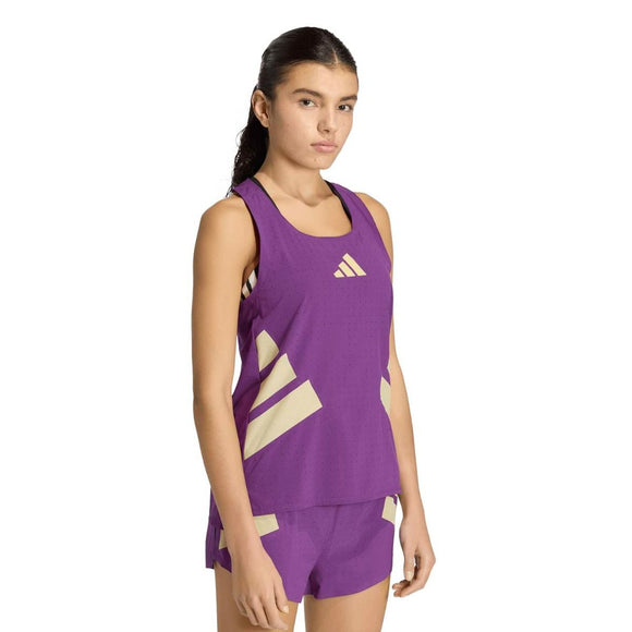En person med langt mørkt hår står med front mod en almindelig hvid baggrund iført en Adidas Rtr Tank, Dame, i violet, sammen med matchende shorts med lyse geometriske striber.