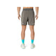 Der ses en person set bagfra, iført Asics Road 2-N-1 7In-shorts til mænd i farven Truffle Grey. Personen har desuden lyse, blågrønne mønstrede sokker og hvide løbesko på. Fokus er på personens lænd og ben foran en ensfarvet hvid baggrund.