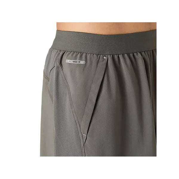 Nærbillede af en person, der bærer Asics Road 2-N-1 7In-shorts i farven Truffle Grey, med elastisk linning, sidepaneler i mesh og et lille ACTIBREEZE-mærke tæt på lommen. Billedet fokuserer på siden af shortsene og en del af taljen og fremhæver de designelementer, der er karakteristiske for Asics’ performance-tøj.