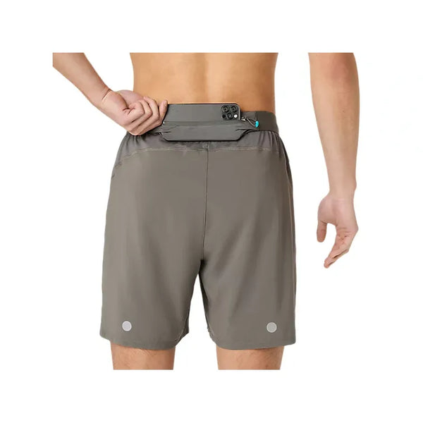 Der ses en person set bagfra iført ASICS Road 2-N-1 7In-løbeshorts til mænd i farven Truffle Grey, der har en baglomme med lynlås, hvor der er plads til en smartphone. Disse løbeshorts har to små reflekterende cirkler tæt på sømmen og tilbyder en komfort, der kan sammenlignes med kompressionsshorts.