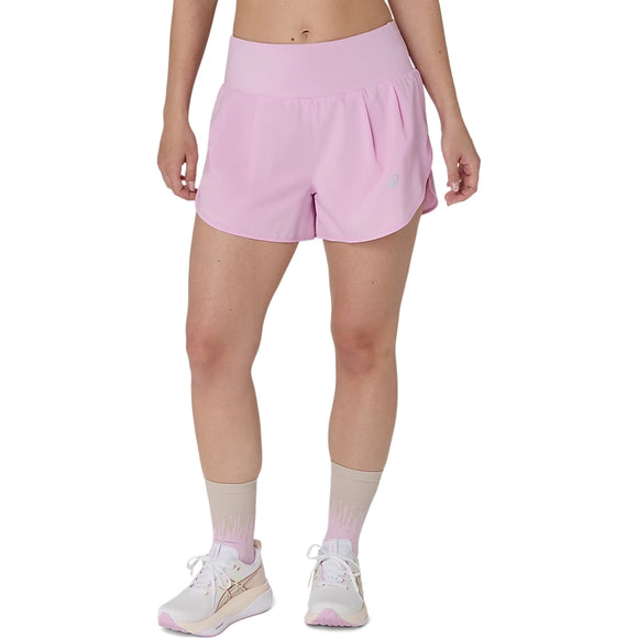 En person har Asics Road 3.5In-shorts til kvinder i farven Hazy Lilac på, beige sokker og hvide sneakers og står foran en ensfarvet hvid baggrund. Kun underkroppen er synlig, hvilket fremhæver det hurtigtørrende design.