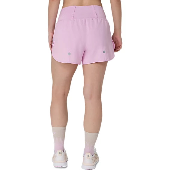 Der ses en person set bagfra iført ASICS Road 3.5In Shorts Dame i farven Hazy Lilac, beige sokker og hvide sneakers. Løbeshortsene til kvinder har to små reflekterende cirkler tæt på sømmen på en ensfarvet hvid baggrund.
