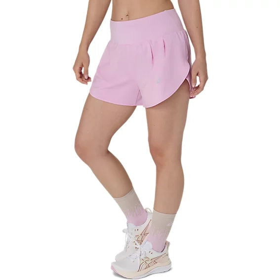 En person står iført ASICS Road 3.5In Shorts Dame i farven Hazy Lilac, beige strømper og hvide sportssko med lyserøde detaljer. Billedet viser personens underkrop foran en ensfarvet hvid baggrund.