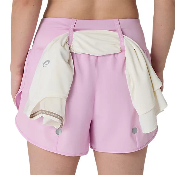 En person iført ASICS Road 3.5In Shorts Dame i farven Hazy Lilac med en hvid skjorte eller jakke, der er trukket gennem linningen bagpå, fotograferet bagfra foran en ensfarvet hvid baggrund.