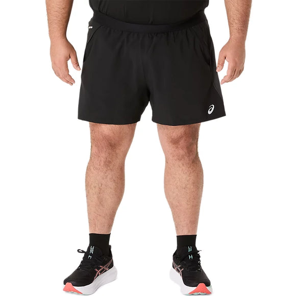 En person står med ansigtet vendt fremad iført ASICS Road 5In-shorts til mænd i farvekombinationen Performance Black/Graphite Grey. Armene hænger afslappet ned langs siden, og looket fuldendes af sorte sokker og sort-hvide løbesko. Den ensfarvede hvide baggrund skaber et rent, minimalistisk udtryk, der fremhæver disse uundværlige løbetøjsprodukter fra ASICS.