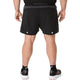 En person iført sorte Asics Road 5In-shorts, Herre i farvekombinationen Performance Black/Graphite Grey, samt sorte sokker og sorte løbesko med hvide såler, står med ryggen til kameraet. Den ensfarvede hvide baggrund fremhæver dette klassiske løbetøj fra Asics.