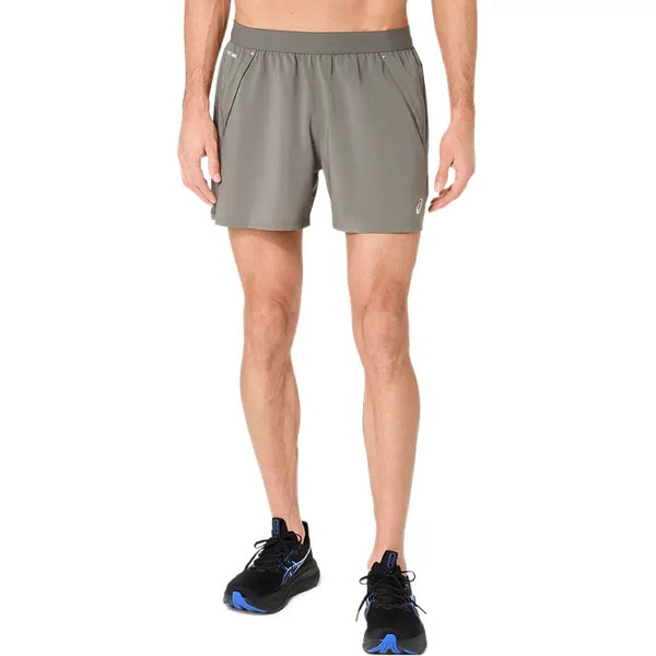 Der vises et billede af en person fra livet og ned, iført Asics Road 5In Shorts, Herre, i farverne Truffle Grey og sorte løbesko, på en ensfarvet hvid baggrund.