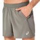 En person har Asics Road 5In Shorts, Herre i farven Truffle Grey på, med elastisk linning og sidelommer. Det hurtigtørrende stof og det synlige Asics-logo tæt på nederkanten sikrer komfort og ydeevne. Den ene hånd hviler i en lomme.