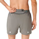 Der ses en person set bagfra iført Asics Road 5In Shorts, Herre, Truffle Grey, som har en lille, delvist åben lomme i linningen og to reflekterende, runde mærker tæt på nederkanten.