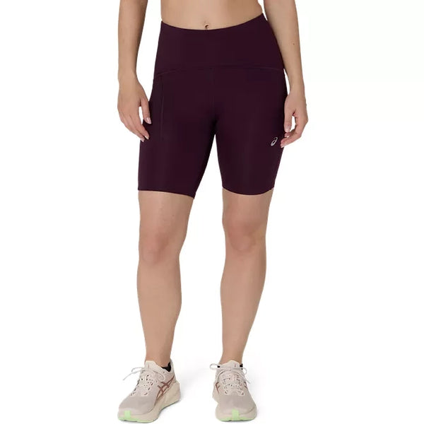 En person har Asics Road High Waist 8In Sprinter, Dame, mørk auberginefarvede tights og beige løbesko på og står foran en ensfarvet hvid baggrund. Personens hoved og underben er ikke synlige.
