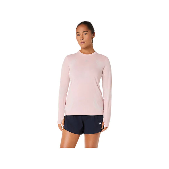 En person står med ansigtet fremad i en Asics Road Seamless LS Top til kvinder i Morganite/Dusty Red, der er fremstillet af genbrugsmaterialer, og mørke marineblå sportsshorts på en almindelig hvid baggrund.