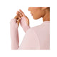 En kvinde i Asics Road Seamless Ls Top, Dame, Morganite/Dusty Red - lavet af genbrugsmaterialer - ses fra siden mod en hvid baggrund. Hun løfter hænderne for at justere et ærme og viser tommelfingerhuller i designet.