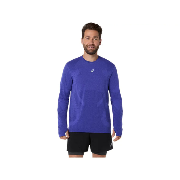 En skægget mand iført en Asics Road Seamless LS Top, Herre, Cobalt Burst/Eggplant lavet af genbrugsmaterialer og sorte shorts står med ansigtet fremad og smiler mod en almindelig hvid baggrund.