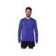 En skægget mand iført en Asics Road Seamless LS Top, Herre, Cobalt Burst/Eggplant lavet af genbrugsmaterialer og sorte shorts står med ansigtet fremad og smiler mod en almindelig hvid baggrund.
