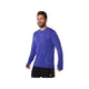 En mand iført en Asics Road Seamless Ls Top, Herre, i Cobalt Burst/Eggplant - lavet af genbrugsmaterialer - og sorte shorts står på en hvid baggrund med ansigtet lidt til siden og smiler.