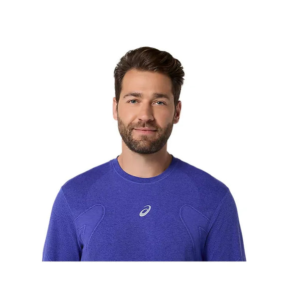 En mand med kort brunt hår og skæg er iført Asics Road Seamless LS Top til mænd i Cobalt Burst/Eggplant. Han står med ansigtet fremad mod en almindelig hvid baggrund.