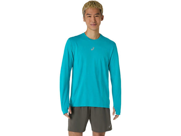 En person står med ansigtet vendt fremad og har ASICS Road Seamless LS Top til mænd i farven Energy Aqua på – en åndbar langærmet trøje med et lille logo på brystet – samt mørkegrå sportsshorts. Baggrunden er ensfarvet hvid.