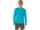 En person står med ansigtet vendt fremad og har ASICS Road Seamless LS Top til mænd i farven Energy Aqua på – en åndbar langærmet trøje med et lille logo på brystet – samt mørkegrå sportsshorts. Baggrunden er ensfarvet hvid.