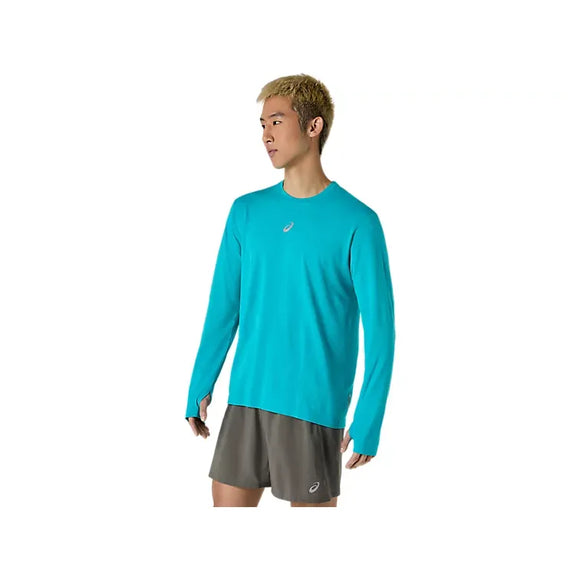 En person med kort, lyst hår har ASICS Road Seamless LS Top, Herre, i farven Energy Aqua på – en åndbar langærmet trøje – kombineret med grå shorts, hvor begge dele er forsynet med ASICS-logoet, mens vedkommende står foran en ensfarvet hvid baggrund.