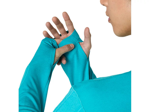 En person, der har en Energy Aqua Asics Road Seamless Ls Top (Herre) på, trækker tommelfingerhullet over sin venstre tommelfinger. Billedet fokuserer på hænderne og trøjen og fremhæver den sømløse løbetrøje, mens en del af personens nedre ansigt er synligt på en hvid baggrund.
