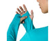 En person, der har en Energy Aqua Asics Road Seamless Ls Top (Herre) på, trækker tommelfingerhullet over sin venstre tommelfinger. Billedet fokuserer på hænderne og trøjen og fremhæver den sømløse løbetrøje, mens en del af personens nedre ansigt er synligt på en hvid baggrund.