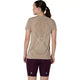 En kvinde står med ryggen til og har en Asics Road Seamless SS Top til kvinder i farven »greige« på, med logo på ryggen og designdetaljer, kombineret med burgunderfarvede sportsshorts på en hvid baggrund – perfekt til løbetøj.