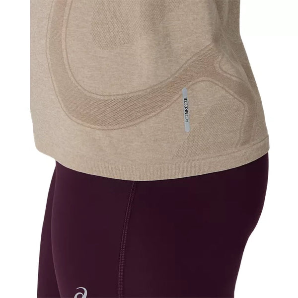 Nærbillede af en person iført en Asics Road Seamless SS Top, Dame, i farven greige, samt mørkerøde leggings. Billedet fremhæver detaljerne ved sidesømmen og den lille reflekterende mærkat på toppen.