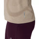 Nærbillede af en person iført en Asics Road Seamless SS Top, Dame, i farven greige, samt mørkerøde leggings. Billedet fremhæver detaljerne ved sidesømmen og den lille reflekterende mærkat på toppen.