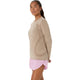 En kvinde poserer foran en hvid baggrund iført en Asics Road Seamless Ss Top, Dame, Greige – en beige, åndbar træningstrøje – kombineret med lyserøde shorts, mens hun kigger let til siden med afslappede arme.