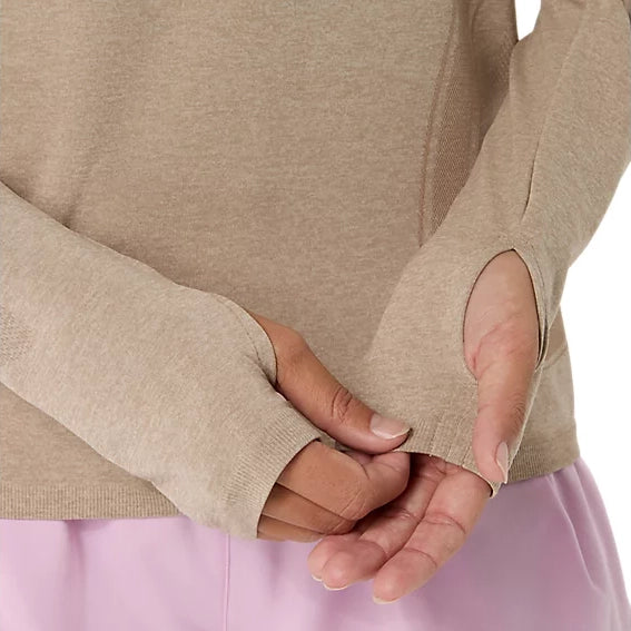 En person har en gråbeige ASICS Road Seamless SS Top til kvinder på – en åndbar træningstrøje med tommelfingerhuller – samt lyserøde bukser og står med armene krydsede foran maven. Kun overkroppen og hænderne ses.