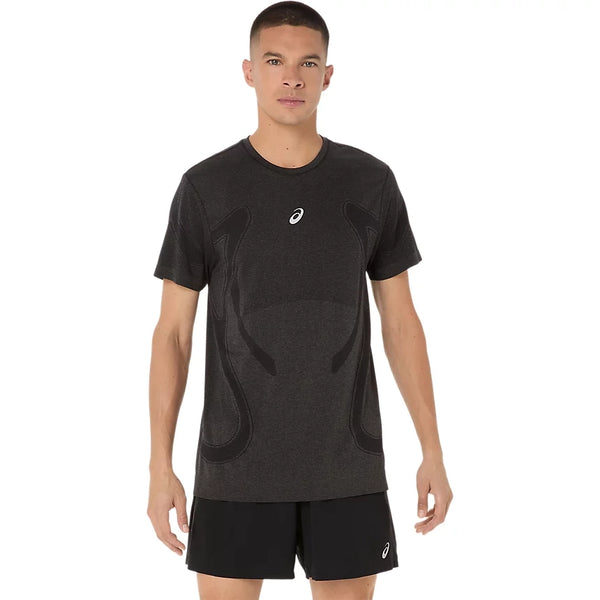 En mand står vendt fremad iført en Asics Road Seamless Ss Top, Herre, i farven Performance Black med et diskret mønster og logo på brystet, kombineret med sorte sportsshorts på en ensfarvet hvid baggrund.
