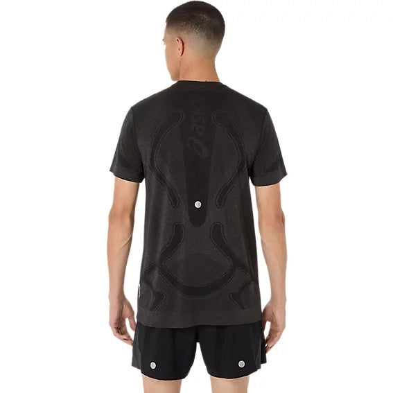 En mand står med ryggen til kameraet og har en Asics Road Seamless Ss Top, Herre, Performance Black på – en kortærmet, svedtransporterende træningstrøje med et abstrakt mønster og lysreflekterende prikker, kombineret med matchende shorts.