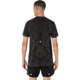 En mand står med ryggen til kameraet og har en Asics Road Seamless Ss Top, Herre, Performance Black på – en kortærmet, svedtransporterende træningstrøje med et abstrakt mønster og lysreflekterende prikker, kombineret med matchende shorts.