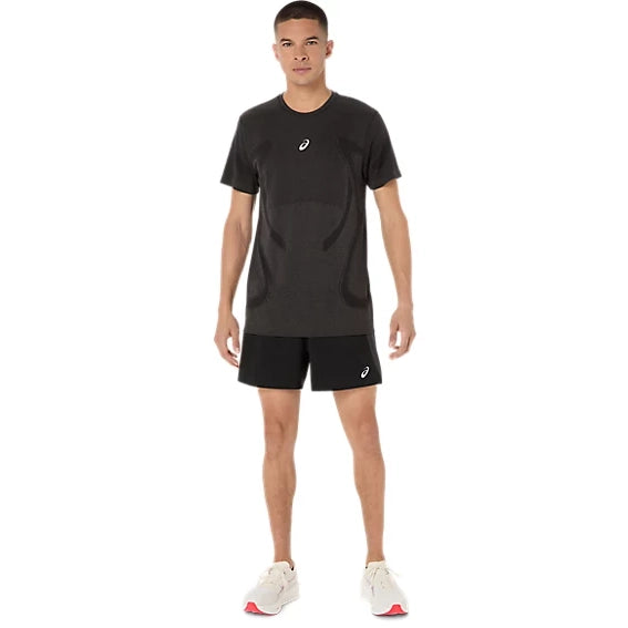 En mand står med ansigtet vendt fremad iført en Asics Road Seamless Ss Top i farven Performance Black og sorte shorts, kombineret med hvide sportssko med røde detaljer, foran en ensfarvet hvid baggrund.