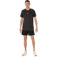 En mand står med ansigtet vendt fremad iført en Asics Road Seamless Ss Top i farven Performance Black og sorte shorts, kombineret med hvide sportssko med røde detaljer, foran en ensfarvet hvid baggrund.