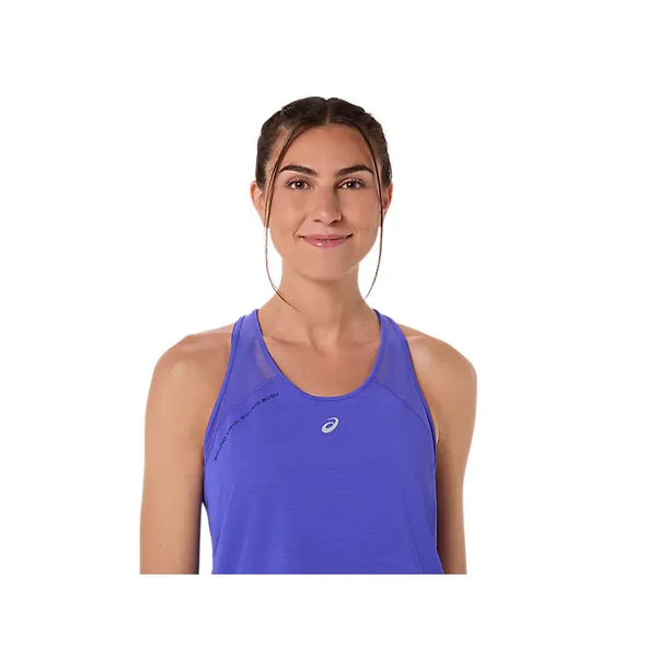 En kvinde med brunt hår i hestehale har en Asics Road Tank, Dame, Cobalt Burst på - kendt for sin åndbarhed - og står mod en hvid baggrund og smiler let.