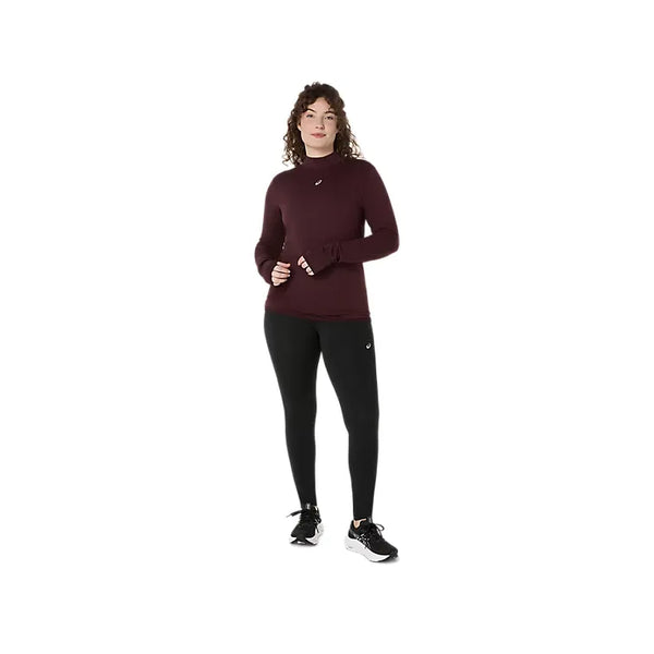 En person med krøllet hår er iført en langærmet, rødbrun sportsbluse og et par ASICS Road Winter High Waist Tights til kvinder i farven Performance Black. Personen står foran en ensfarvet hvid baggrund og ser fremad med hænderne hvilende tæt ved hofterne.