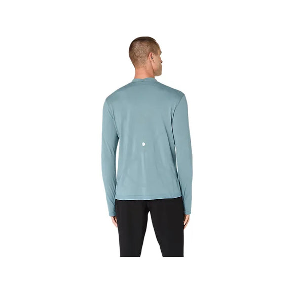 En person står med ryggen til og har en Asics Road Winter Seamless LS Top til mænd i farven »Foggy Teal« på samt sorte bukser. Denne langærmede trøje, der er fremstillet af termomateriale, har en lille hvid prik øverst på ryggen. Baggrunden er ensfarvet hvid.