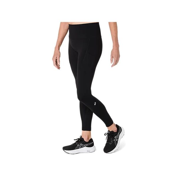 Der vises et billede af en person fra livet og ned, iført et par Asics Road Seamless Tight, Dame, i farven Performance Black – løbetights til kvinder med høj talje og sidelommer – kombineret med sorte løbesko, stående foran en hvid baggrund.