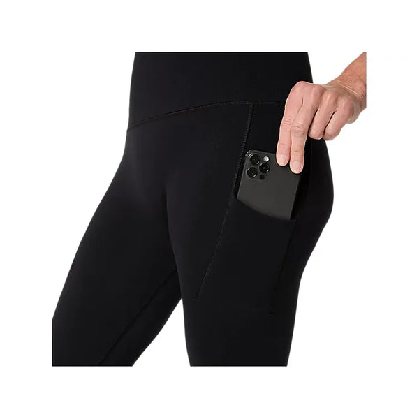 En person, der har ASICS Road Seamless Tight, Dame, Performance Black på, lægger en smartphone ned i sidelommen på sit højre lår. Billedet fokuserer på lommeberegningen og hånden, der holder telefonen.