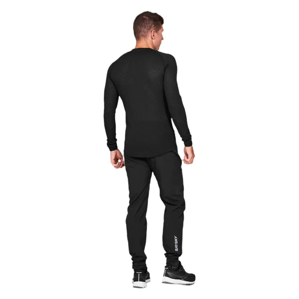 En mand kigger væk, iført Saysky Mesh Base Layer LS i sort og matchende bukser med hvid tekst på højre ben, sammen med sorte sportssko. Dette svedtransporterende unisex-outfit skiller sig ud mod en almindelig hvid baggrund.