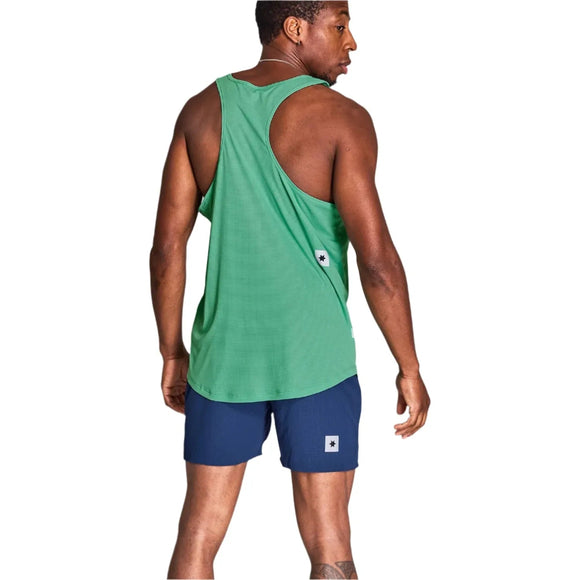 En mand kigger væk og er iført en Saysky Reactive Flow Singlet, Herre, Green Aop lavet af genbrugspolyester og marineblå shorts. Begge har små rektangulære tags. Den ensfarvede baggrund er hvid.